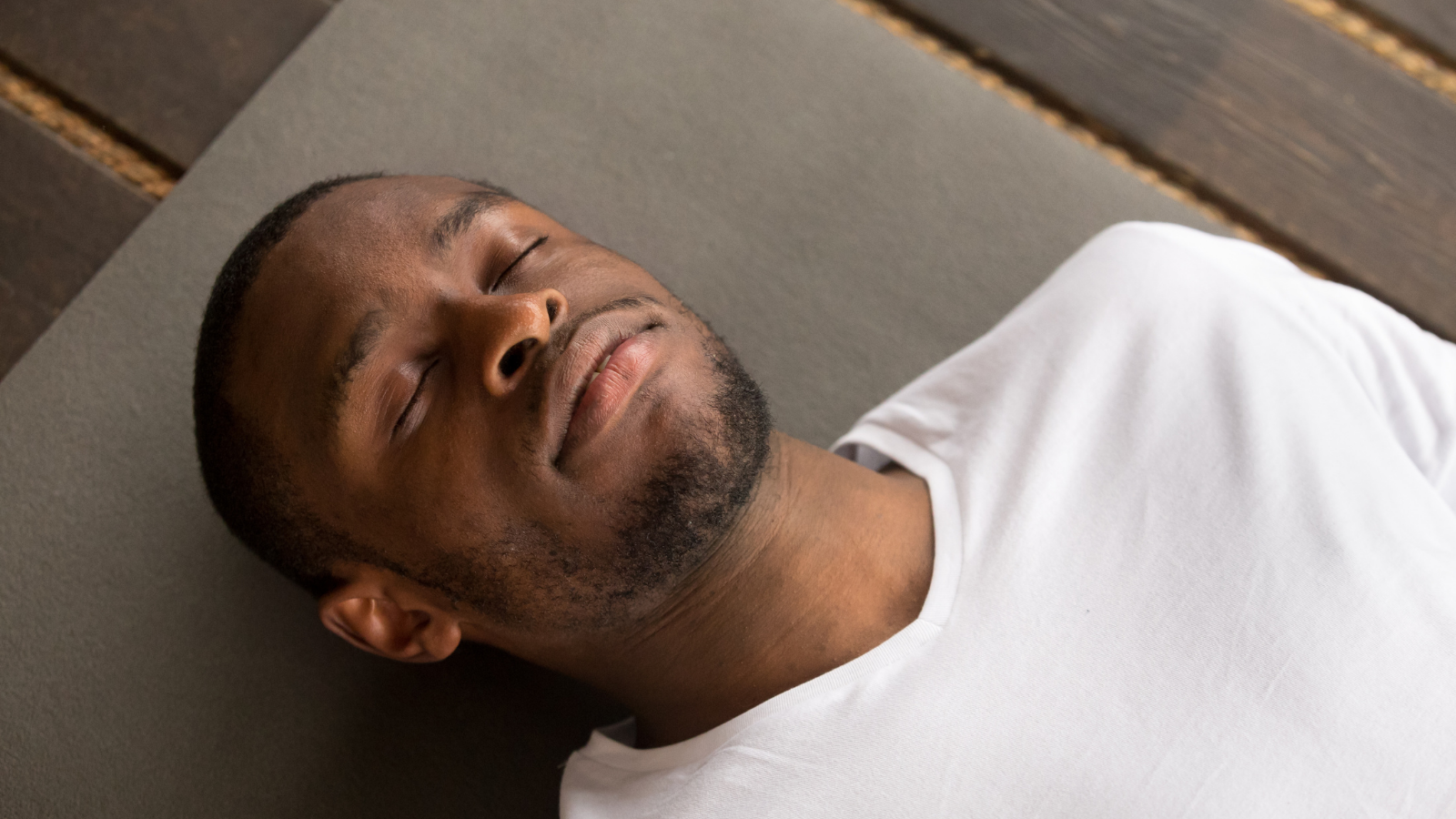 Photo of young black man lying in Savasana or Corpse Pose with his eyes closed