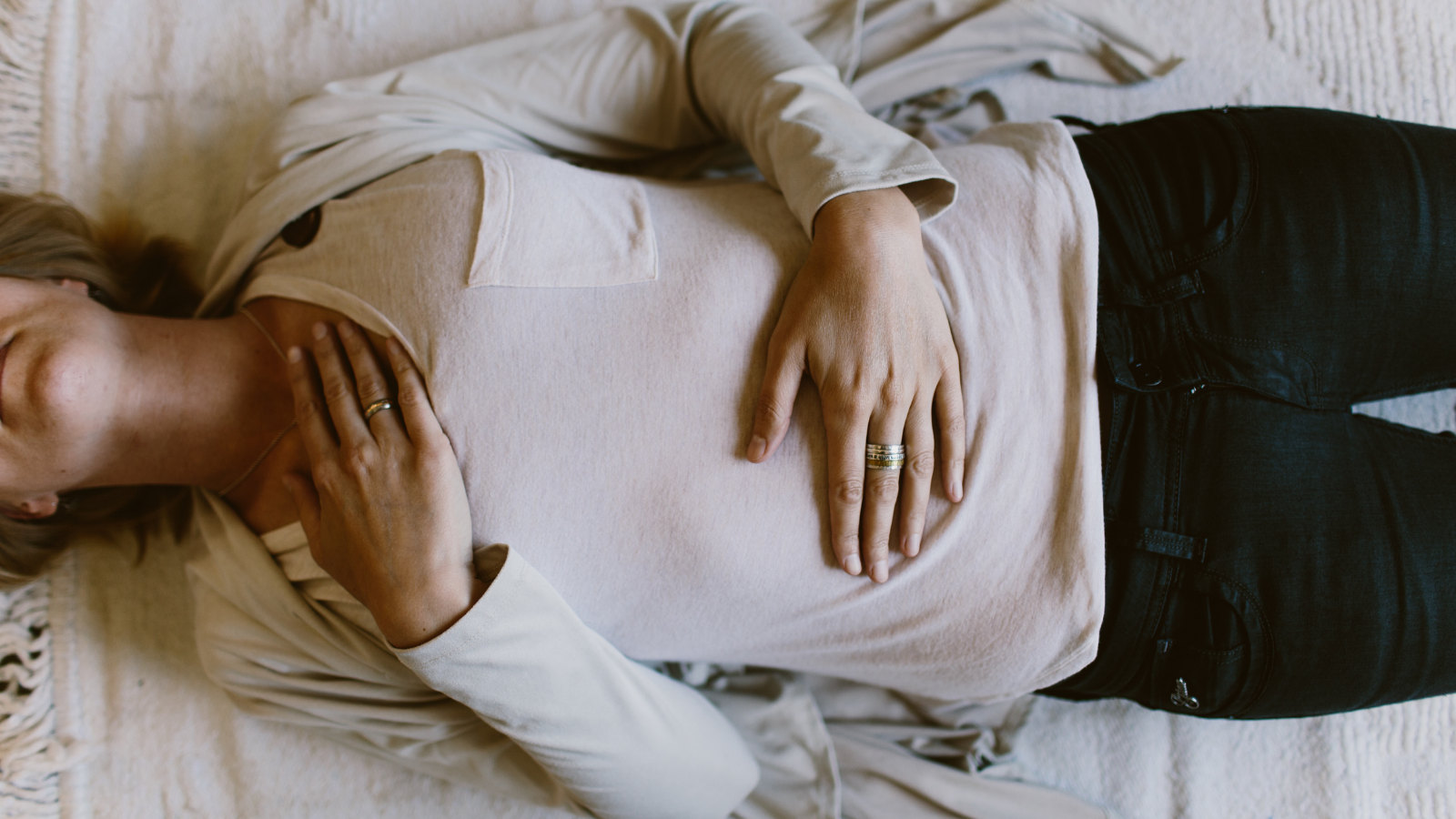 A woman lying down with her hands placed on her heart and her belly in a gesture of self-healing.