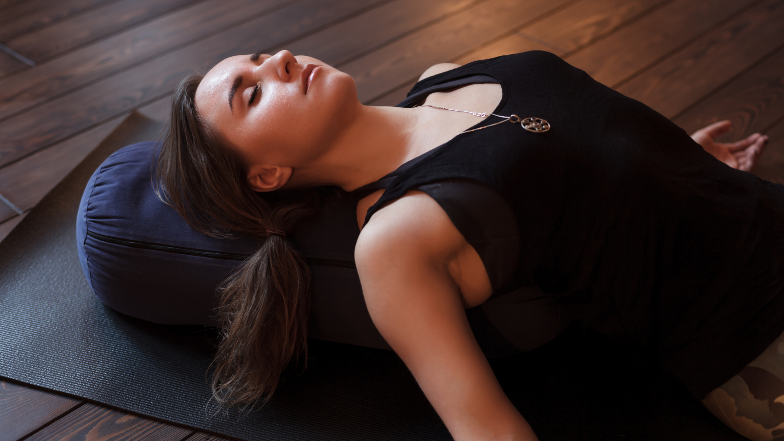 Woman resting after a yoga class in Savasana Pose with bolster under her for supported spine stretch. 