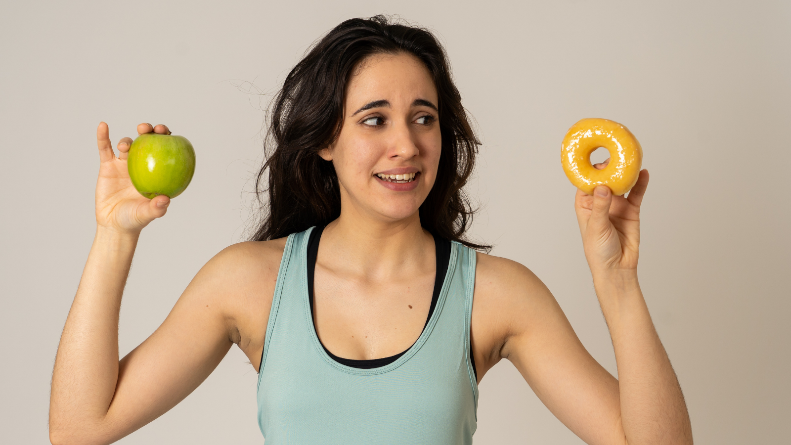 Beautiful young fit woman tempted having to make choice; apple and doughnut, healthy or unhealthy food