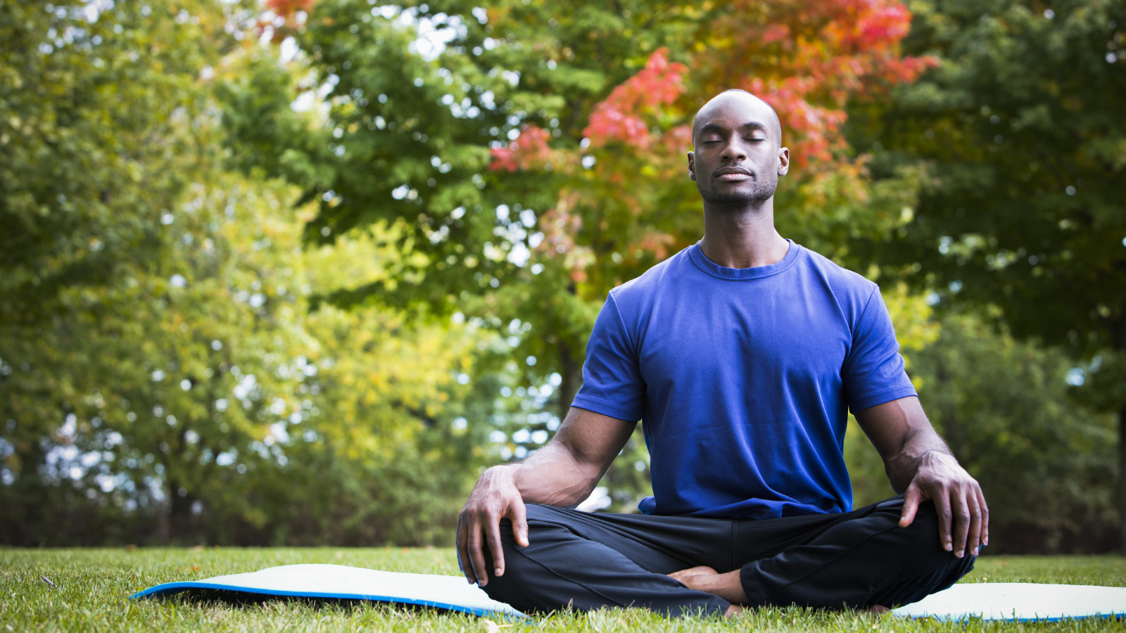 young black man wearing athletic wear sitting in the park doing yoga meditation, a somatic approach to exercise