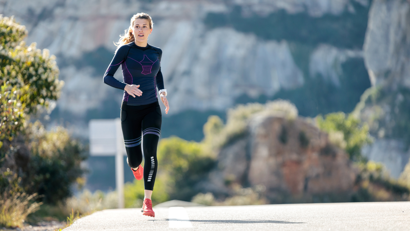 Sporty young woman running on mountain road in beautiful nature, somatic approach to exercise