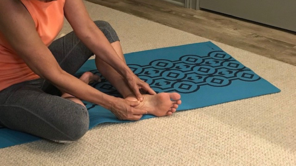 A person practicing foot massage on a yoga mat
